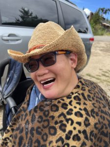 Mikelle in a cowboy hat in the mountains wearing a cheeta poncho.