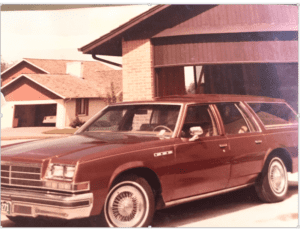 Suburban home with large 1979 brown station wagon in the drive way.
